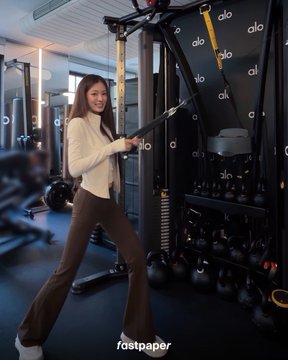 A woman in a gym performs an exercise using TRX-style straps attached to a rack branded with the 'alo' logo, with the watermark 'rostpaper' at the bottom.