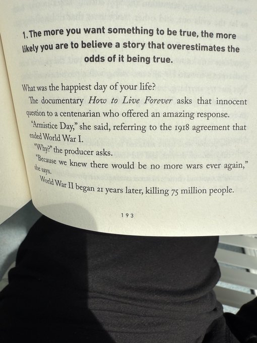An open book page displaying the heading '1. The more you want something to be true, the more likely you are to believe a story that overestimates the odds of it being true' and a story about a centenarian's happiest day being Armistice Day in 1918.