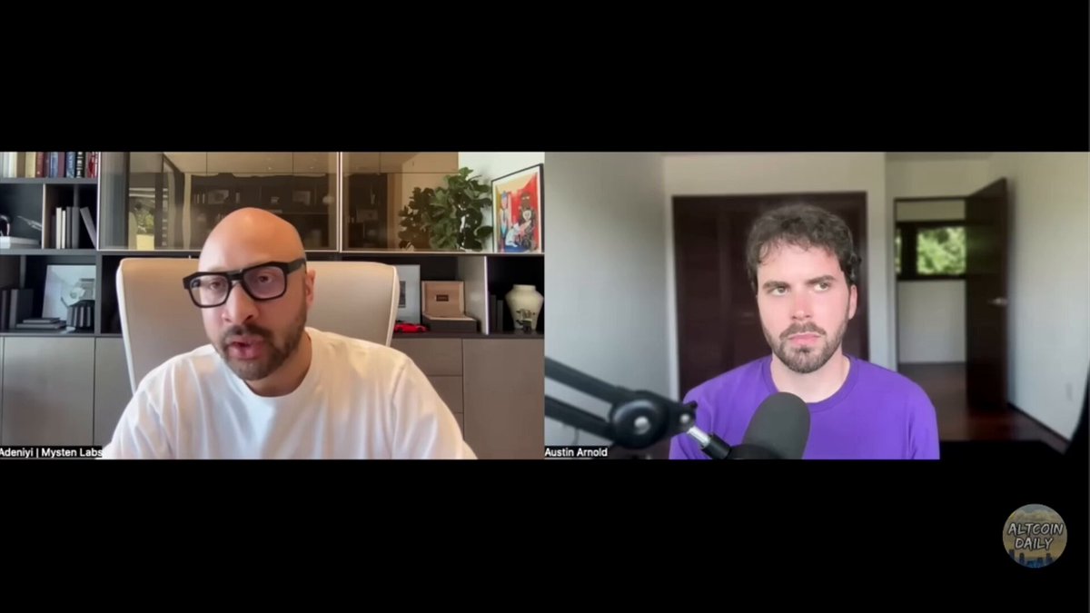 The image shows two men talking into a microphone, with one man wearing glasses and the other wearing a purple shirt. The background of the image features a bookshelf filled with various items such as books and vases. There are also several books visible in the scene. The image is related to the post because it contains information about SUI (Social Trading Infrastructure) and how it enables free stablecoin transactions, which can potentially change the way people invest their money.