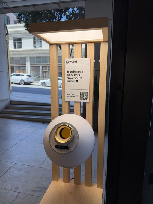 A Worldcoin orb sits outside a boba shop on a wooden stand displaying the message "In an internet full of bots, prove you're human" with a QR code prompting users to scan to get started, exemplifying the San Francisco tech presence the post critiques.