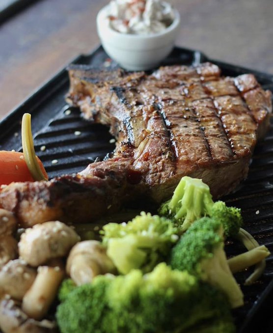 A grilled T-bone steak served on a black grill platter with broccoli, mushrooms, and a side of dipping sauce. The meal represents a solid value for the 0.8 SOL paid—definitely not a "rug pull" given the generous portion of steak and vegetables.