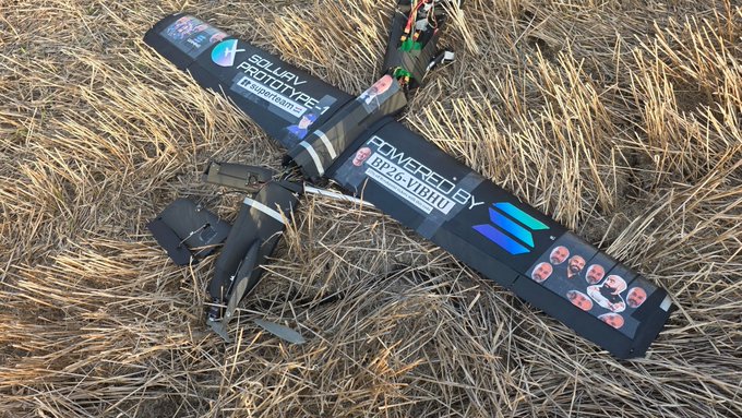 A crashed “Powered by NitroFly” drone lies tangled in dry grass with its propellers and wiring damaged. The joke relates to the post’s claim that the Solana-based team is “shilling Vibhu’s Breakpoint code” but needs to stop launching batteries into the sky.