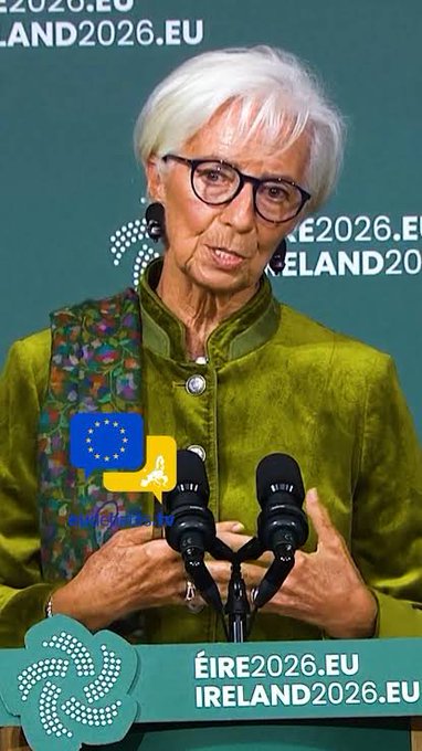 An elderly woman with short white hair and glasses speaking at a podium with the backdrop 'ÉIRE2026.EU / IRELAND2026.EU', suggesting an Ireland 2026 promotional event.