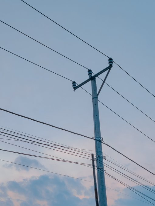 A tall utility pole stretches upward against a pastel sky, its dark power lines radiating outward like silent threads of a network—mirroring the conceptual "Silent Lines" NFT artwork and its ten exclusive editions tied to XTZ. The stark geometry of the wires evokes the quiet, connective infrastructure of modern digital exchange.