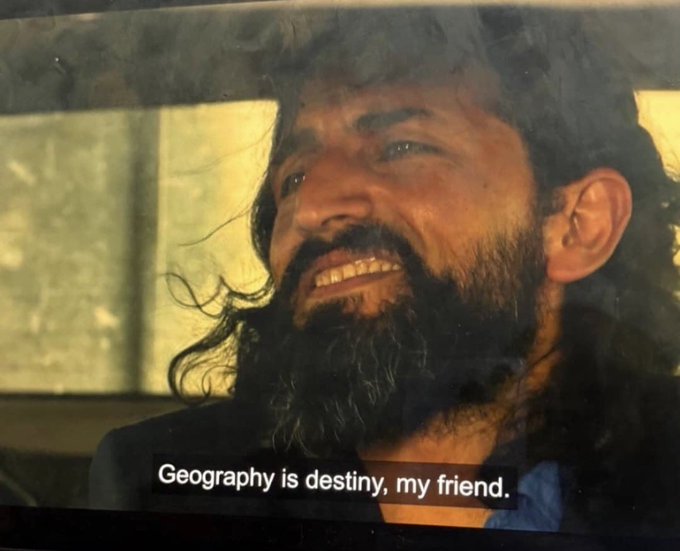 A scene showing a bearded man with long dark hair speaking, with the subtitle 'Geography is destiny, my friend.' visible at the bottom.