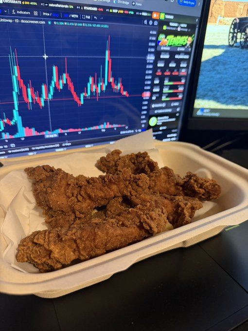 A plate of golden-brown fried chicken tenders in a styrofoam container placed in front of a computer monitor displaying a cryptocurrency trading chart on Crosshair.