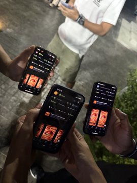 Three people hold up their smartphones, displaying a dark-themed trading interface with candlestick charts and chart patterns, at what appears to be an evening event with greenery visible in the background—illustrating the post's enthusiasm for introducing Jupiter Exchange to attendees at the Superteam Thailand gathering.