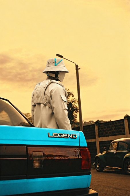A figure in a white bucket hat and backpack stands beside a bright blue car labeled 'LEGEND' at sunset, with a vintage Volkswagen Beetle parked nearby.