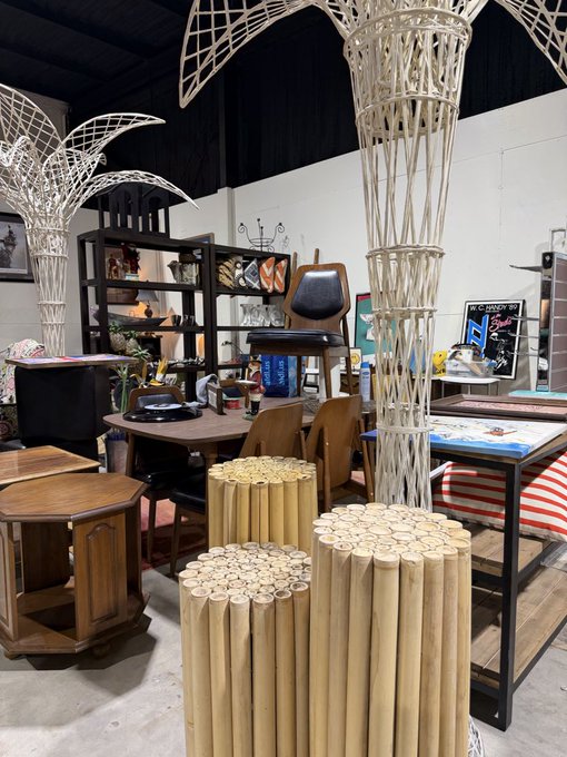 A photograph of an antique or vintage store interior showcasing various items including bamboo stools, wooden furniture, a chair, and decorative metal sculptures.