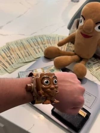 A hand wearing a Fu Manchu (Mushu) character bracelet sits next to fanned-out stacks of cash and a Mr. Potato Head figure in the background.