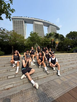 A group of casually dressed friends poses on stone steps in front of the iconic Marina Bay Sands hotel in Singapore, with one person in the foreground playfully lounging while others give thumbs-up gestures. The caption promotes a privacy-focused running app during Token2049, suggesting the image captures attendees from the crypto conference taking a relaxed moment after late-night networking.