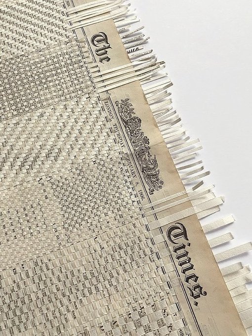 An intricate paper artwork made from woven strips of The New York Times newspaper pages, with the word 'Times' visible across the top sections.