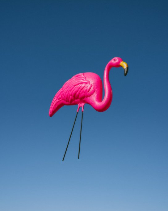 A vibrant pink flamingo lawn ornament with long black legs and a yellow beak stands against a clear blue sky.