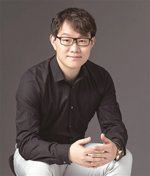 A man wearing glasses and a black dress shirt sits against a gray background with his hands resting on his lap, projecting a professional demeanor. The image accompanies a post discussing the concept of blockchain "landing," where profits from cryptocurrency speculation are shifted into traditional business investments as a practical application of the technology.