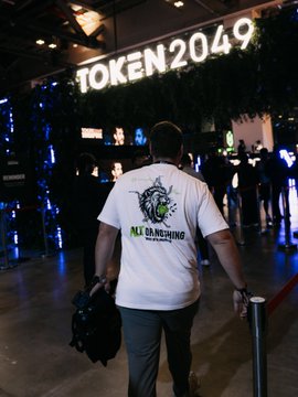 A man wearing a "ILL DUNGHEE" t-shirt walks through the TOKEN2049 conference venue, with the event's illuminated signage visible overhead, capturing the bustling networking atmosphere referenced in the post.
