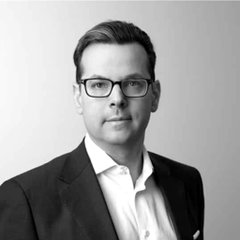 A professional black-and-white headshot features a man wearing glasses and a dark suit jacket over a white shirt, presented against a light background—likely representing an executive or team member associated with the Ripple Delta One launch announcement.
