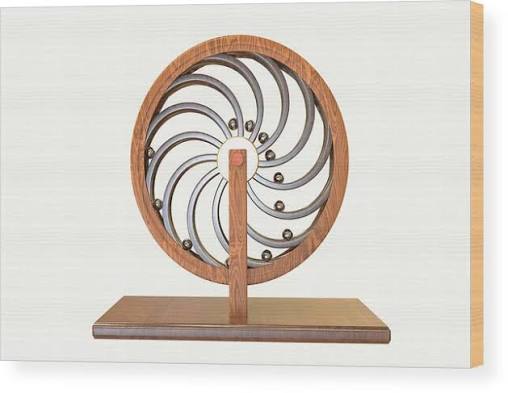 A wooden decorative kinetic sculpture with a circular metal frame containing spiraling metal arms holding small balls, mounted on a wooden base and displayed as wall art.