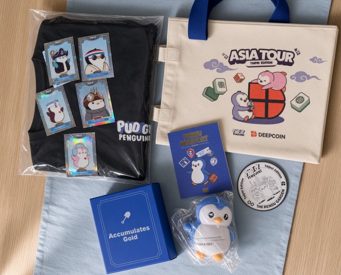 An 'Asia Tour Taipei Edition' merchandise collection laid out on a light surface, featuring a tote bag, plush penguin, t-shirt, and stickers branded with 'PUDGY PENGUINS' and 'DEEPCOIN'.