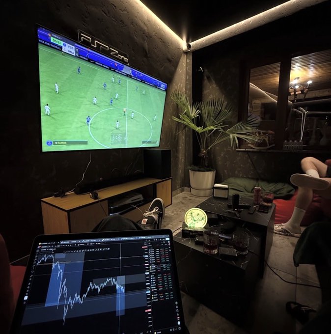 A person relaxes on a couch with their feet up, watching a soccer match on TV while monitoring financial charts on a laptop displaying "SPOT"/"ROBO" tickers, with an "FUTZone" sign visible above the screen. The image conveys a leisurely trading setup, aligning with the post's casual giveaway offer to a new follower.