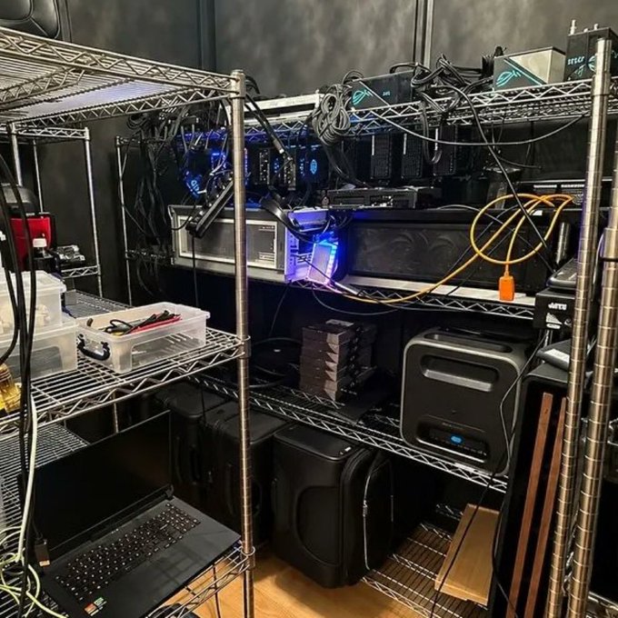 A metal wire shelving unit holding various computer equipment including laptops, monitors, NAS drives, tangled cables, and what appears to be cryptocurrency mining rigs.