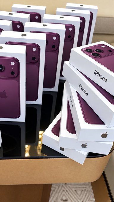 Multiple boxes of purple iPhones are stacked in a cardboard container, showing the distinctive camera module and Apple logo on the packaging.