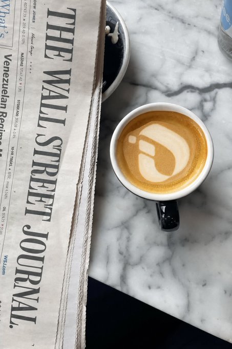 A cappuccino with latte art sits on a marble surface beside a copy of The Wall Street Journal, suggesting a morning reading routine paired with a coffee break—setting a sophisticated, business-focused tone fitting for the "GM, Linkers!" market commentary about InterLink and related tickers.