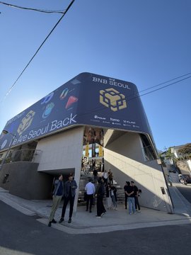 An exterior view of an 'HNB SEOUL' building with signage reading 'Seoul, Korea' and 'Have a Seoul Back', where several people are gathered at the entrance.