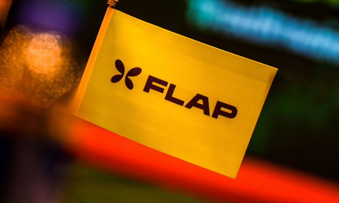 A yellow flag bearing the "FLAP" logo is prominently displayed against a vibrant, blurred background of orange and green lights, visually reinforcing the platform's community-driven branding and launch tools ecosystem.