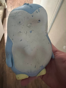 The underside of a handcrafted clay sculpture resembling a chubby blue and white character, held in someone's hand.
