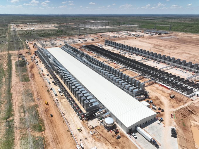An aerial view of Galaxy Digital's Helios data center campus showing rows of transformers and infrastructure under a large white-roofed building, illustrating the massive scale of the 1.63 GW facility described in the post. The sprawling industrial site with electrical equipment ready for service visually represents the $GLXY Phase I milestone of delivering 133MW of operational power ahead of typical industry wait times.