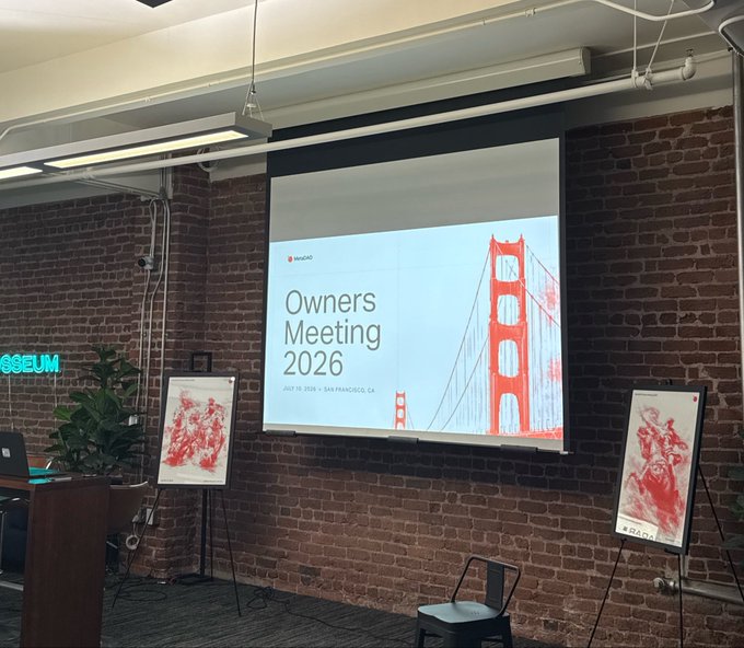 The image shows an event space with a projection screen displaying "Owners Meeting 2026" by MetaDAO, scheduled for July 19, 2026, in San Francisco, CA, alongside an illustration of the Golden Gate Bridge. This setting ties to the MetaDAO Conference mentioned in the post, where discussions about the future of better ownership took place, and where Umbra shared upcoming announcements.