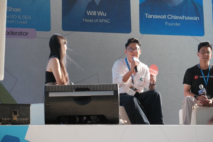 A panel discussion at what appears to be a cryptocurrency or fintech conference, with speakers including Wil Wu (Head of APAC) and Tanawat Chiewhawan (Founder) seated on stage while one man speaks into a microphone. The post's message about making cryptocurrency funds truly flow connects to the discussion shown, suggesting the panelists are addressing real-world financial applications beyond just trading digital assets.