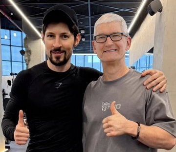 Two men pose together with thumbs up in what appears to be a gym setting; the younger man wears a black Gymshark cap and shirt, while the older man wears glasses and a gray t-shirt.