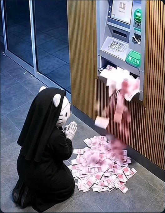 A masked individual dressed in black kneeling before an ATM as pink banknotes spew out onto the ground.