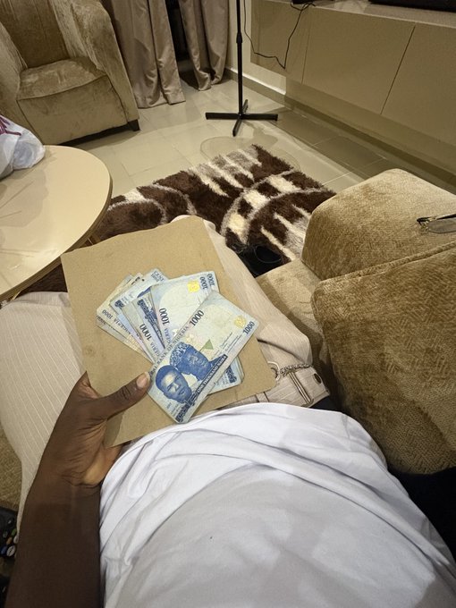 A person holds a fan of Nigerian 1000 naira banknotes in their hand while sitting on a couch in a living room, celebrating receiving cash as a gift for attending an IRL web3 event.