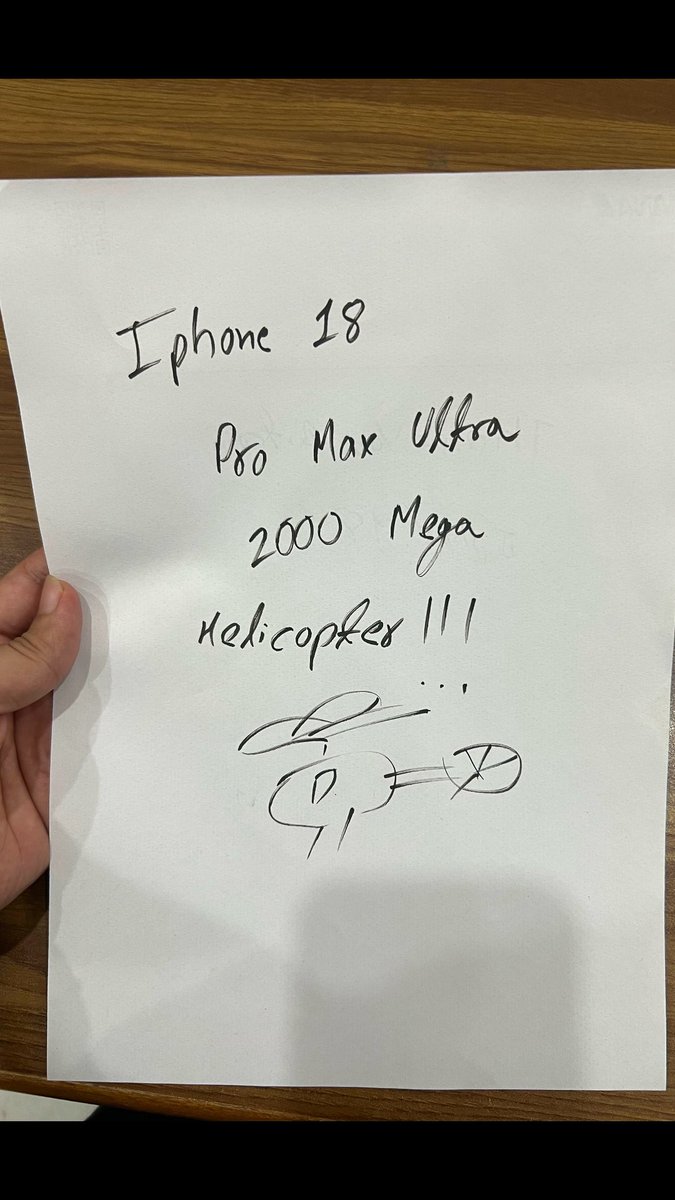 A hand holds a handwritten note that reads "Iphone 18 Pro Max Ultra 2000 Mega Helicopter 111" followed by a crude sketch of a helicopter.