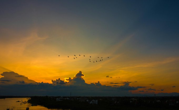 The image shows a beautiful sunset over a body of water with birds flying overhead. The sky is filled with warm hues of orange, yellow, and blue as the sun sets behind the horizon. There are several birds soaring through the sky, creating a sense of movement and life in the scene. The image also contains text that reads "Good evening everyone Your @NucleusCodes reputation is being built right now, even while you rest. And one of the best campaigns to put it to work? The @quipnetwork Quantum Echoes NFT collection  1,000 Eigen Keys powered by true quantum randomness". This text seems to be related to the image or could be part of a caption that accompanies the photo.