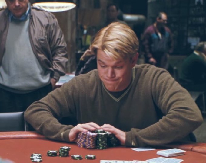 A scene from the movie Rounders showing a young blonde man in a brown sweater sitting at a red poker table, looking down at a stack of chips.