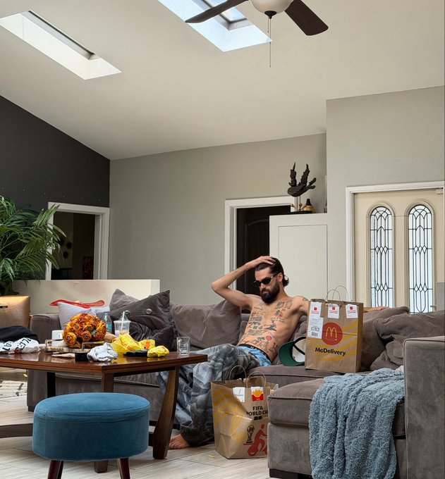 A shirtless, tattooed man wearing sunglasses lounges on a couch amid scattered takeout bags from McDonald's and a "Fiesta World" bag, capturing a lazy post-festive vibe. The "SOLANA SUMMER" caption playfully ties into the laid-back, sun-soaked atmosphere, with the Solana logo hinting at a crypto-themed summer celebration.