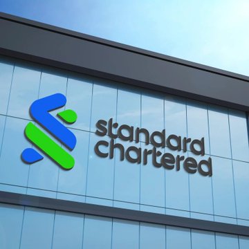 The image features the logo of Standard Chartered bank, a financial institution, displayed on the exterior of a building with blue glass paneling.