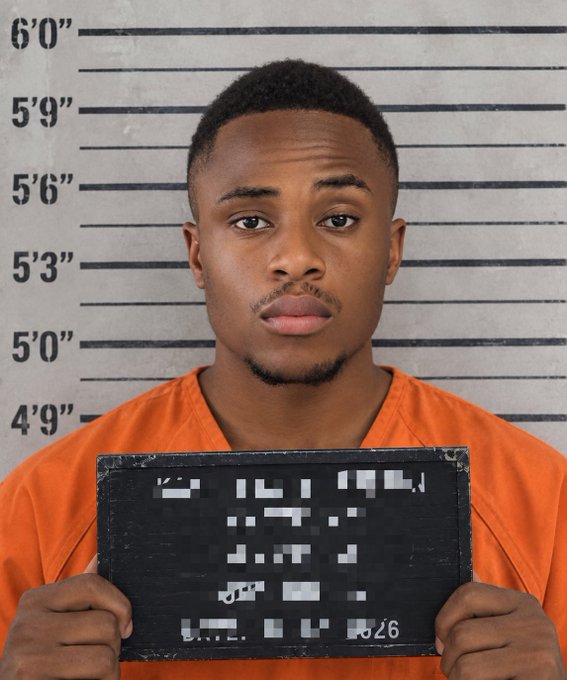 A mugshot of a young man in an orange jumpsuit holding a blackboard, standing against a height chart background.