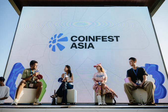 Four panelists sit on stage at CoinFest Asia, with a large screen behind them displaying the "COINFEST ASIA" logo alongside the event's blue and green graphics. The image illustrates the accompanying post about a panel discussion featuring representatives from Tether, Dash, and MOI Technology on the future of on-chain activity and AI agents.