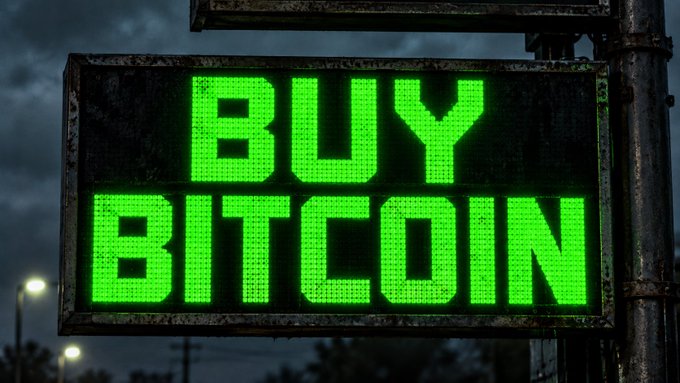 An illuminated green LED sign displaying "BUY BITCOIN" against a dark evening sky.
