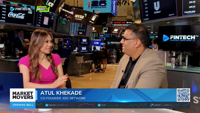 A screenshot from 'FINTECH TV' showing a 'Market Movers' interview segment featuring a woman and 'ATUL KHEKADE, CO-FOUNDER, XDC NETWORK' on the floor of the NYSE, with stock tickers for Nasdaq, US30, and EURUSD displayed.