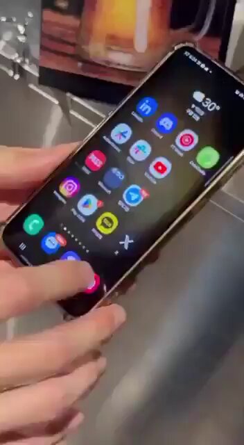 The image features a person holding up their phone displaying various app icons including social media apps like Instagram and Facebook. The phone's screen also shows that $XRP has been officially added as a payment method via Surfy, which is a South Korean payment gateway service. This information was shared on social media platforms, indicating the widespread adoption of this new payment method in the country.
