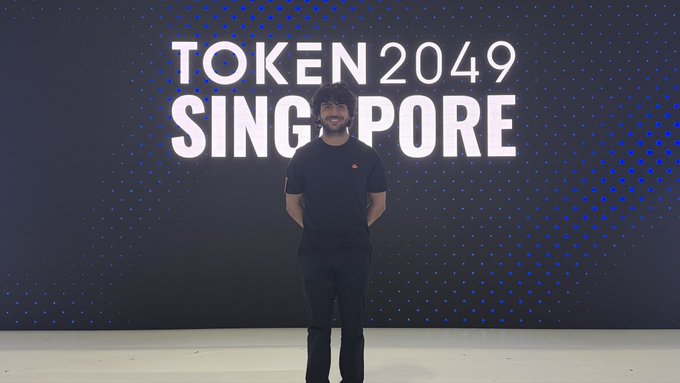 A person stands in front of a backdrop reading "TOKEN 2049 SINGAPORE" at the crypto conference. The "fox sighting" caption likely refers to a fox-like figure or branding in the background, suggesting the person may be associated with a fox-themed crypto project.