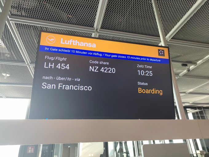 A Lufthansa airport departure board displaying flight LH 454 (code share NZ 4220) to San Francisco, with a status of 'Boarding' and a time of 10:25.