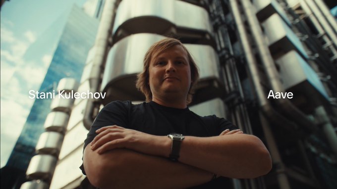 Stani Kulechov, labeled “Aave,” stands with his arms crossed in front of a futuristic metallic building. The text highlights Aave’s role in modernizing outdated financial-system rails ahead of the full episode tomorrow.