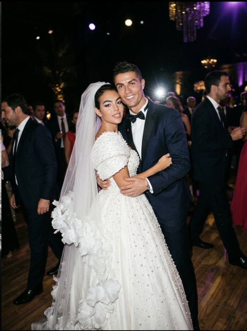 Cristiano Ronaldo poses in a dark tuxedo alongside his partner Georgina Rodríguez, who is wearing an elaborate white wedding gown and veil.