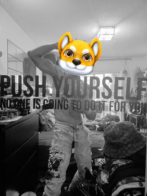 A shirtless person poses in a messy bedroom with an emoji covering their face, standing in front of a wall that reads "PUSH YOURSELF NO ONE IS GOING TO DO IT FOR YOU." The motivational imagery aligns with the post's choice of the $OMIKAMI token, reinforcing a self-driven, perseverance-themed crypto pick.